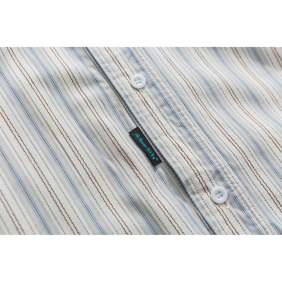Close-up of a cream shirt front with blue and brown stripes, white buttons, and a small sewn-in tag.