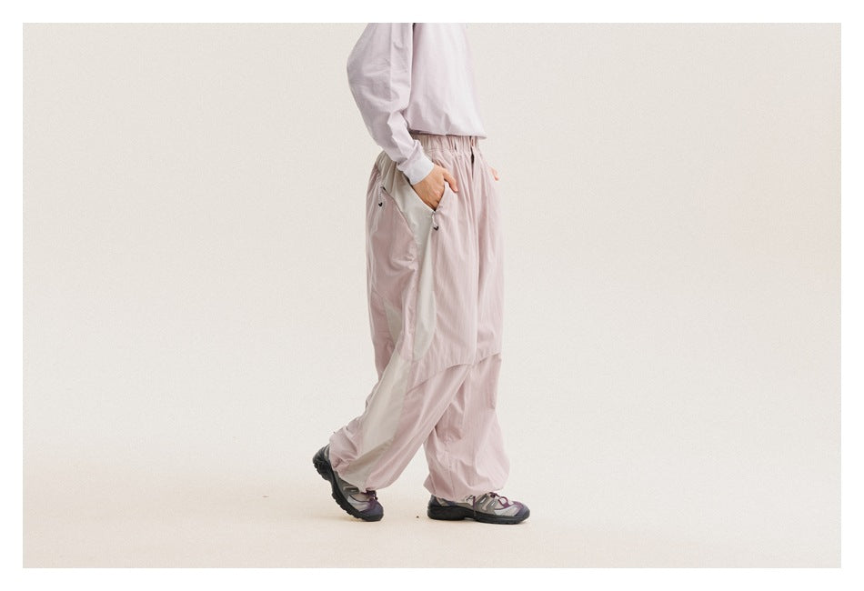 Side view of a model wearing loose pale mauve pants with contrasting light side panels and an elastic waist.