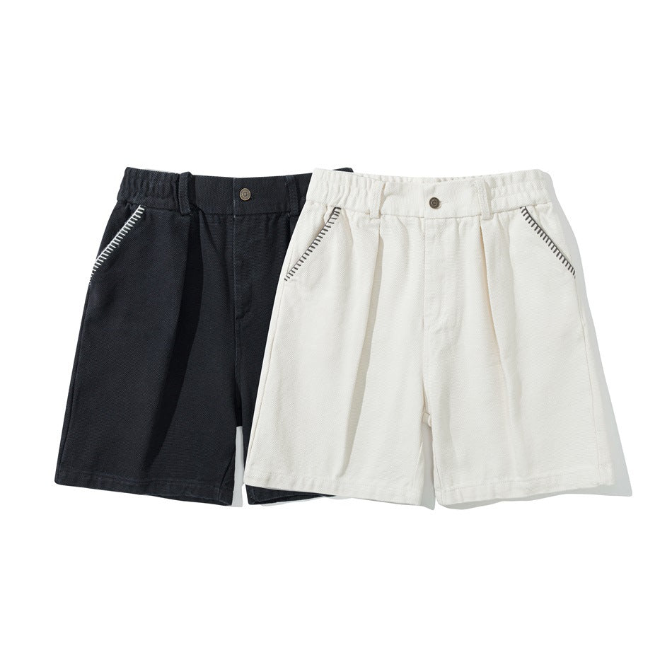 Front view of black and ivory shorts side by side, with pleated fronts and contrast stitching at the pocket openings.