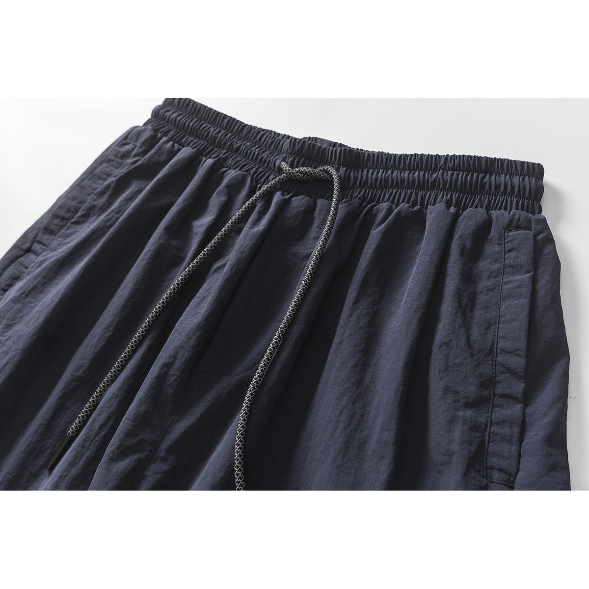 Close-up of navy pants showing the elastic waistband, braided drawcord, and side pocket opening.
