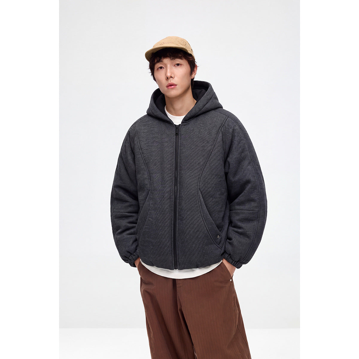 Model wearing a charcoal gray hooded zip-up jacket with curved front pockets and gathered cuffs.