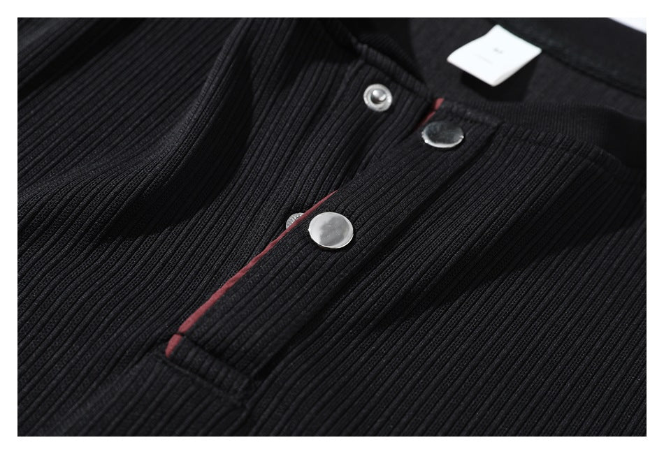 Close-up of a black ribbed garment's snap-button placket with a narrow red edge accent.