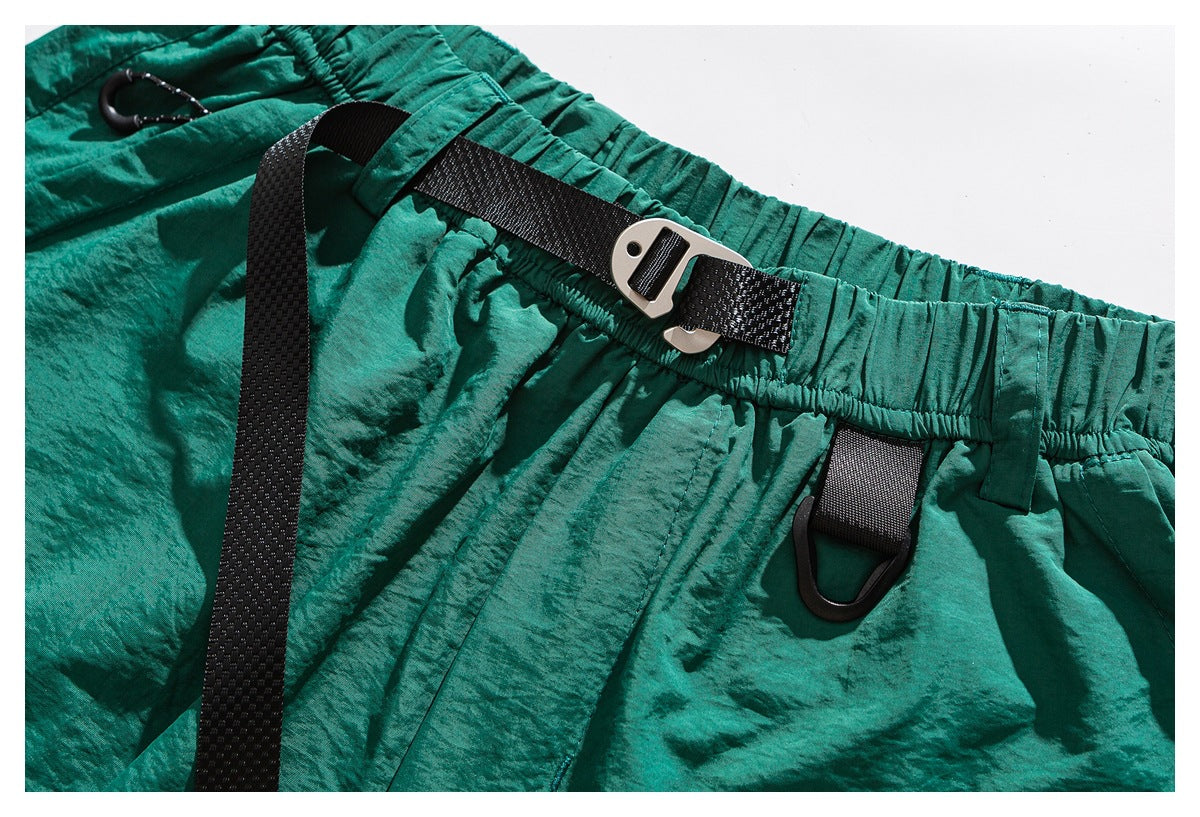 Close-up of teal shorts showing an elastic waistband, black webbing strap, buckle and hanging loop.