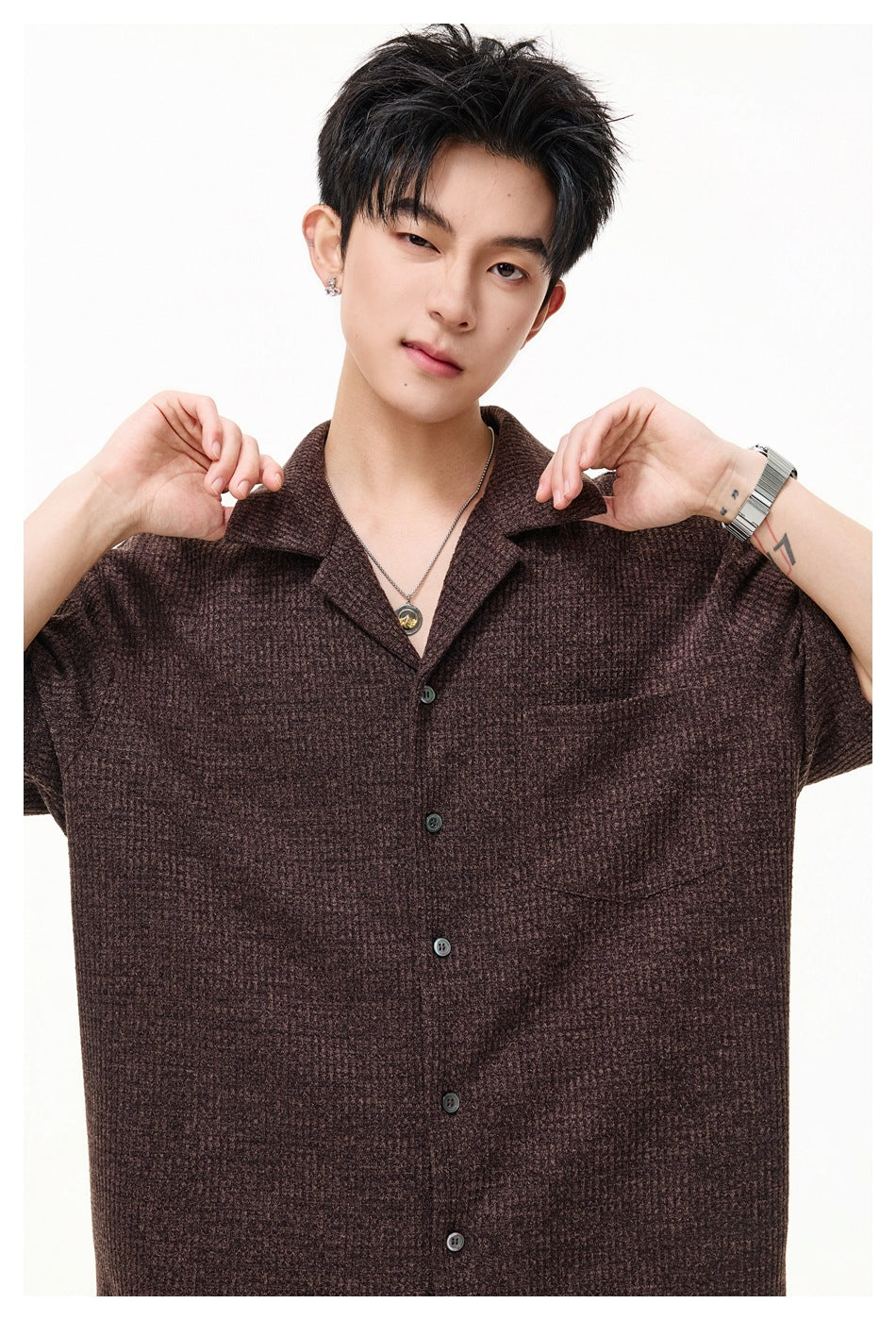 Close view of a model wearing a brown textured short-sleeve button-up shirt with a notched collar and chest pocket.