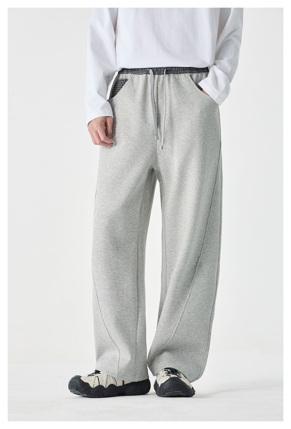 Person wearing gray wide-leg pants with plaid waistband and one hand in pocket, with white top and sneakers