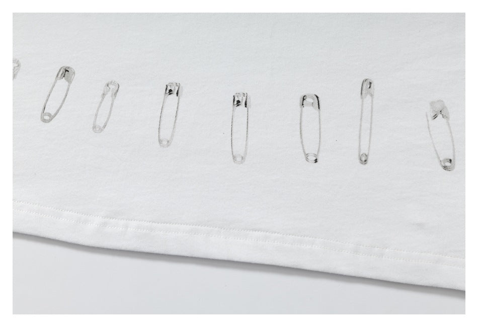 Close-up of a white shirt hem with a row of safety-pin illustrations printed above the stitching.