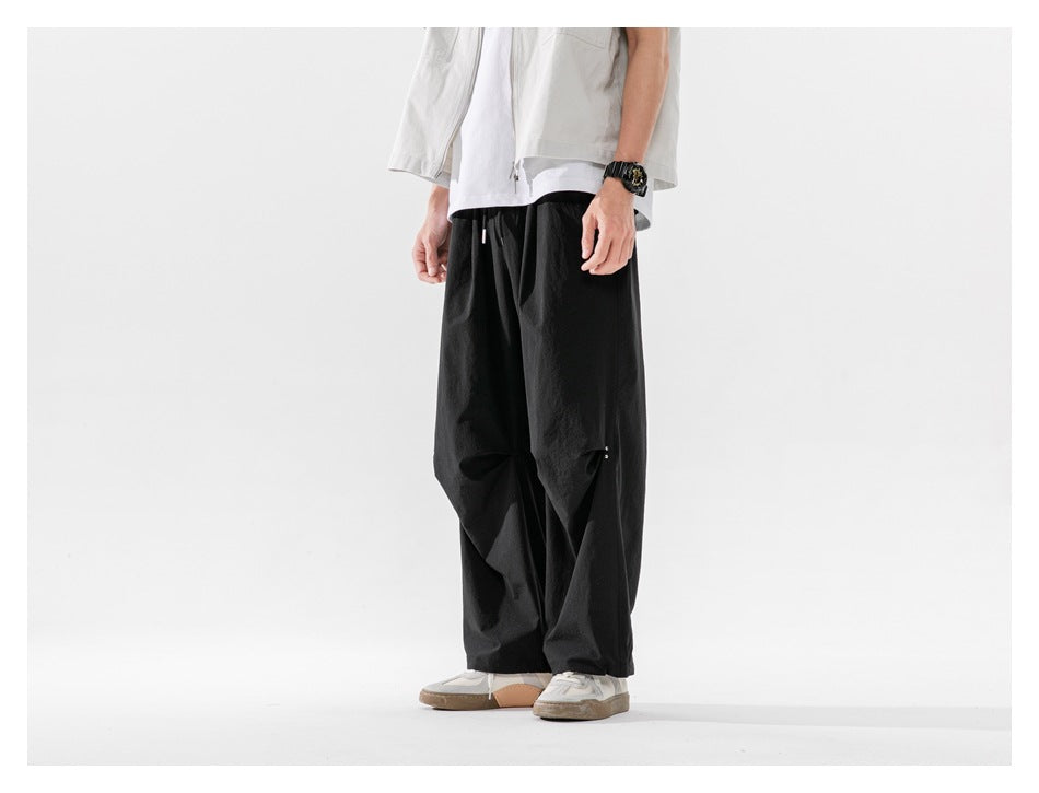 Side three-quarter view of black wide-leg pants with knee pleat detail worn with sneakers and a light vest