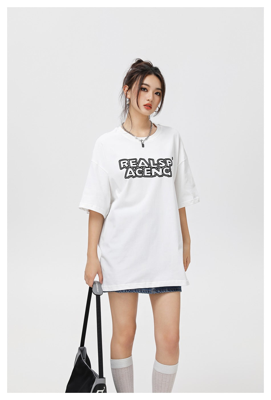 Closer front view of a model wearing an oversized white T-shirt with bold black chest lettering.