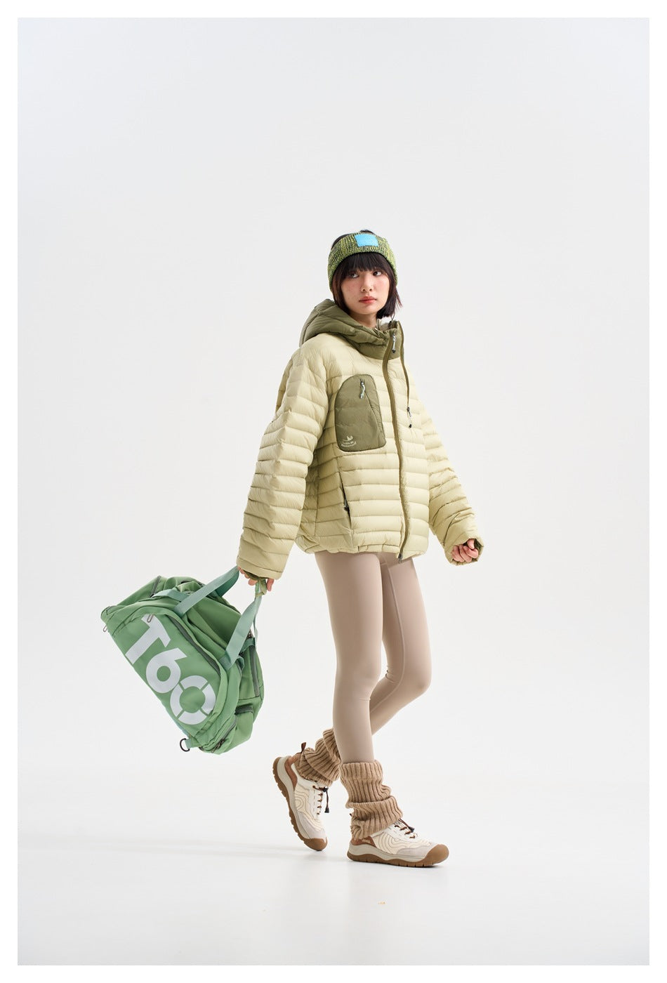 Full-length model wearing a cream quilted jacket and carrying a green duffel bag.