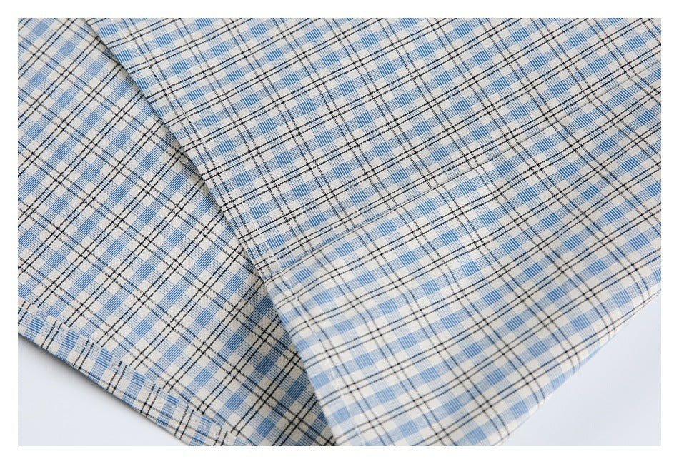 Close-up of folded light blue, white, and black plaid shirt fabric with a stitched edge.