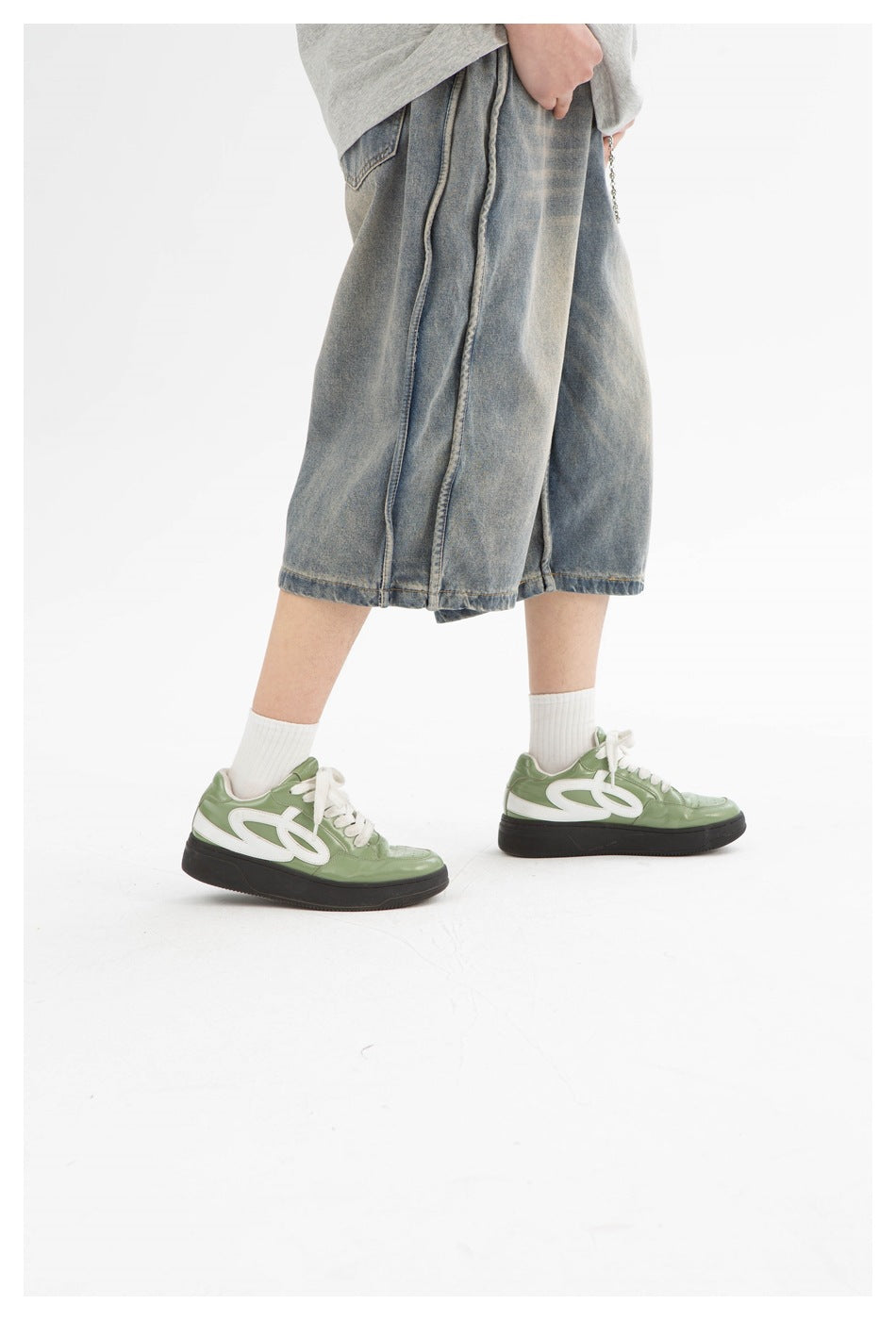 Side view of loose washed denim shorts with wide legs, paired with white socks and green sneakers.