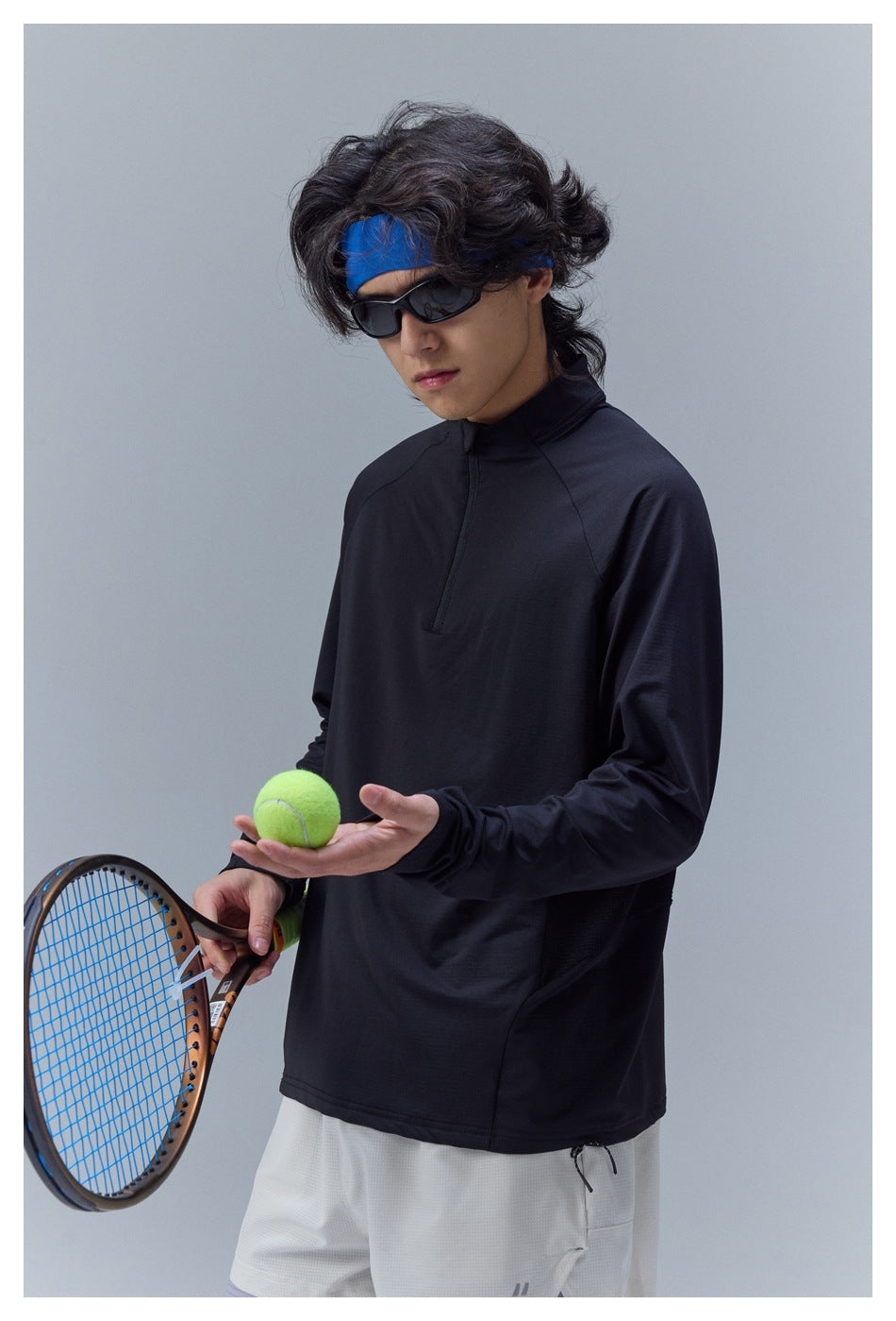 Close view of a model wearing a black long-sleeve quarter-zip tennis top, with light shorts partly visible.