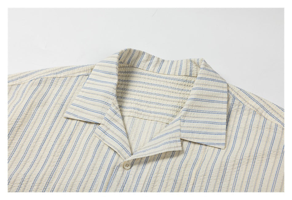 Close-up of a cream shirt collar and upper placket with fine blue and tan stripes.
