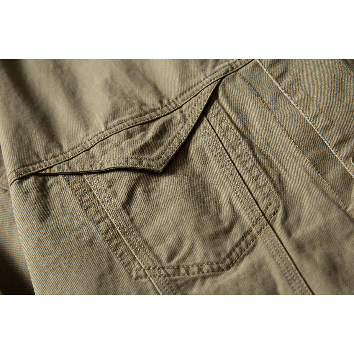 Close-up of the olive-khaki jacket's pointed chest pocket and double-stitched seams.