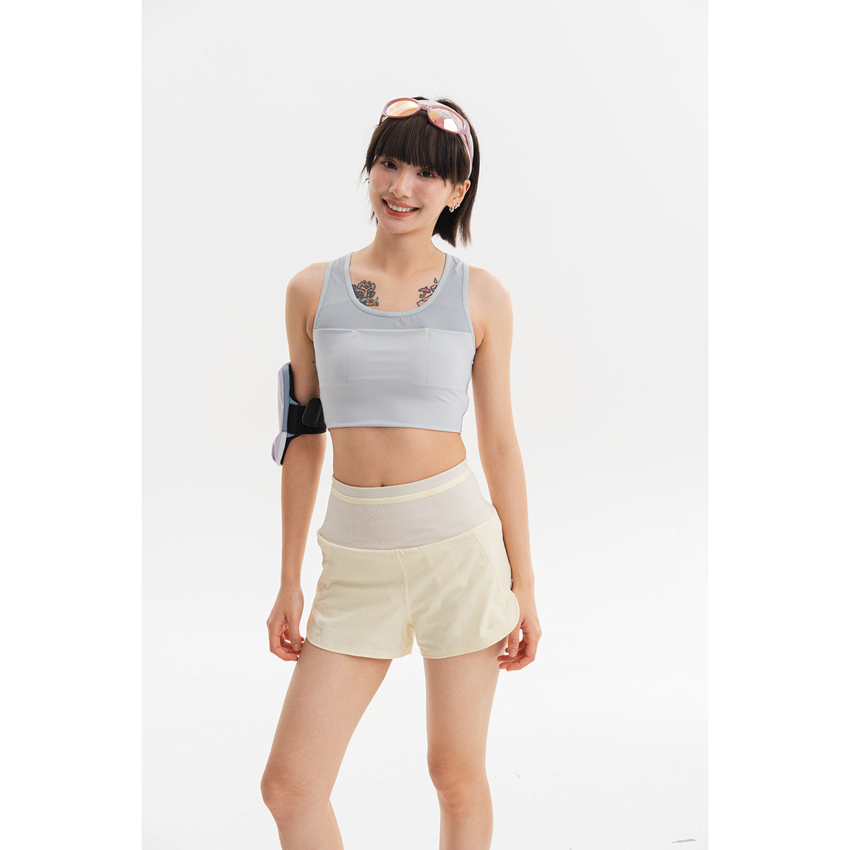 Model wearing a pale gray cropped sports top and cream shorts, with an armband against a white background.