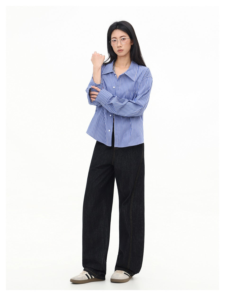 Model wearing a blue-and-white striped button-front shirt with long sleeves and dark wide-leg jeans.