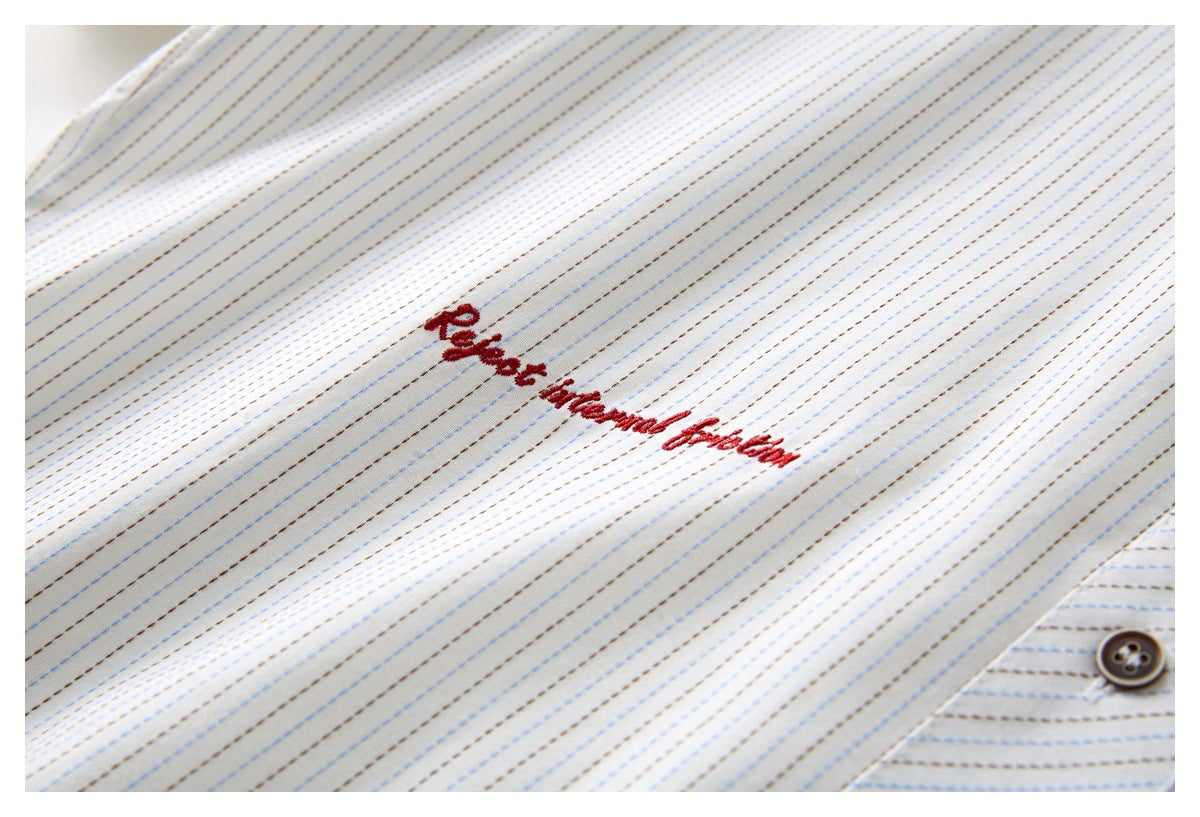 Close-up of a white shirt with fine blue and brown stripes, red cursive embroidery, and a dark button.