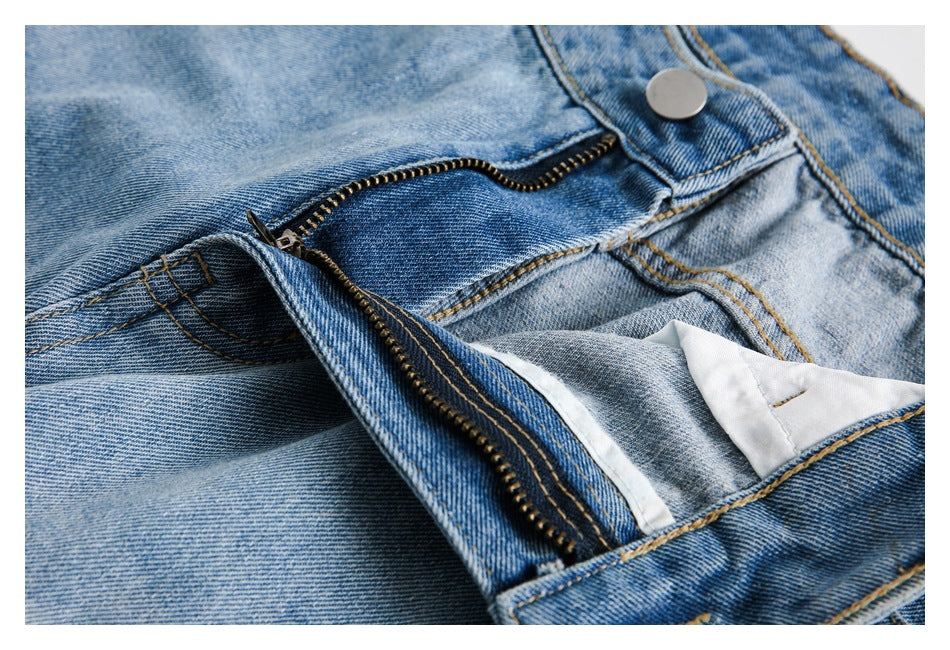 Close-up of light blue jeans showing the metal button, open zipper fly, and contrast stitching.