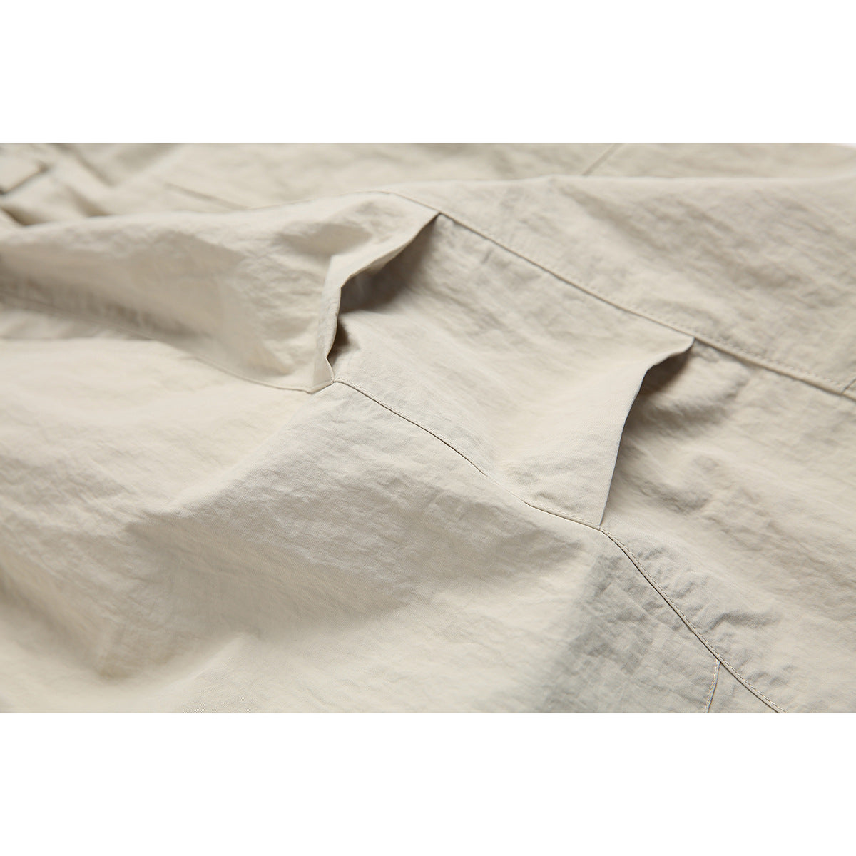 Close-up of beige shorts showing a layered cargo pocket and stitched panel seams.