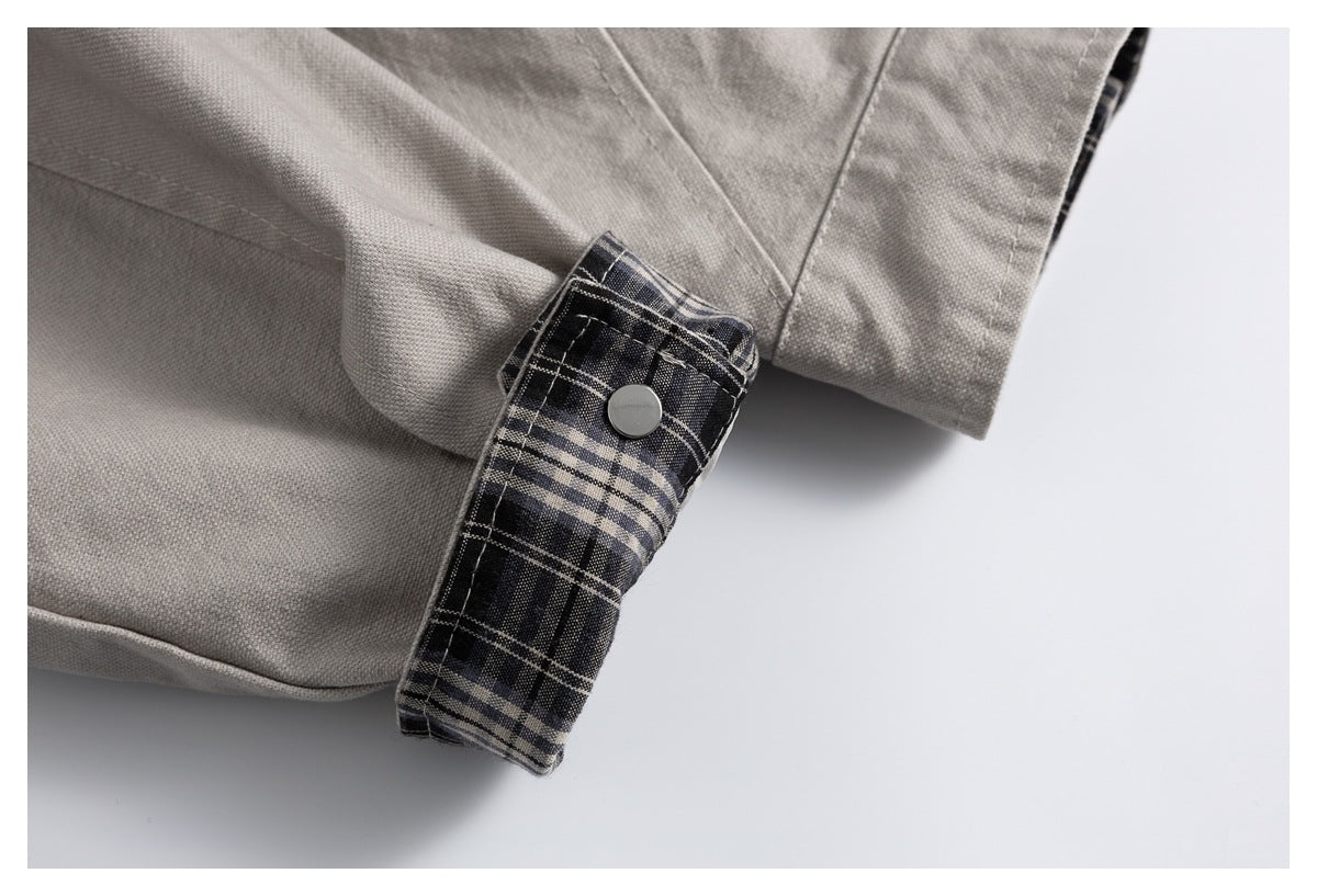 Close-up of a light gray garment cuff with dark plaid lining and a silver snap button.