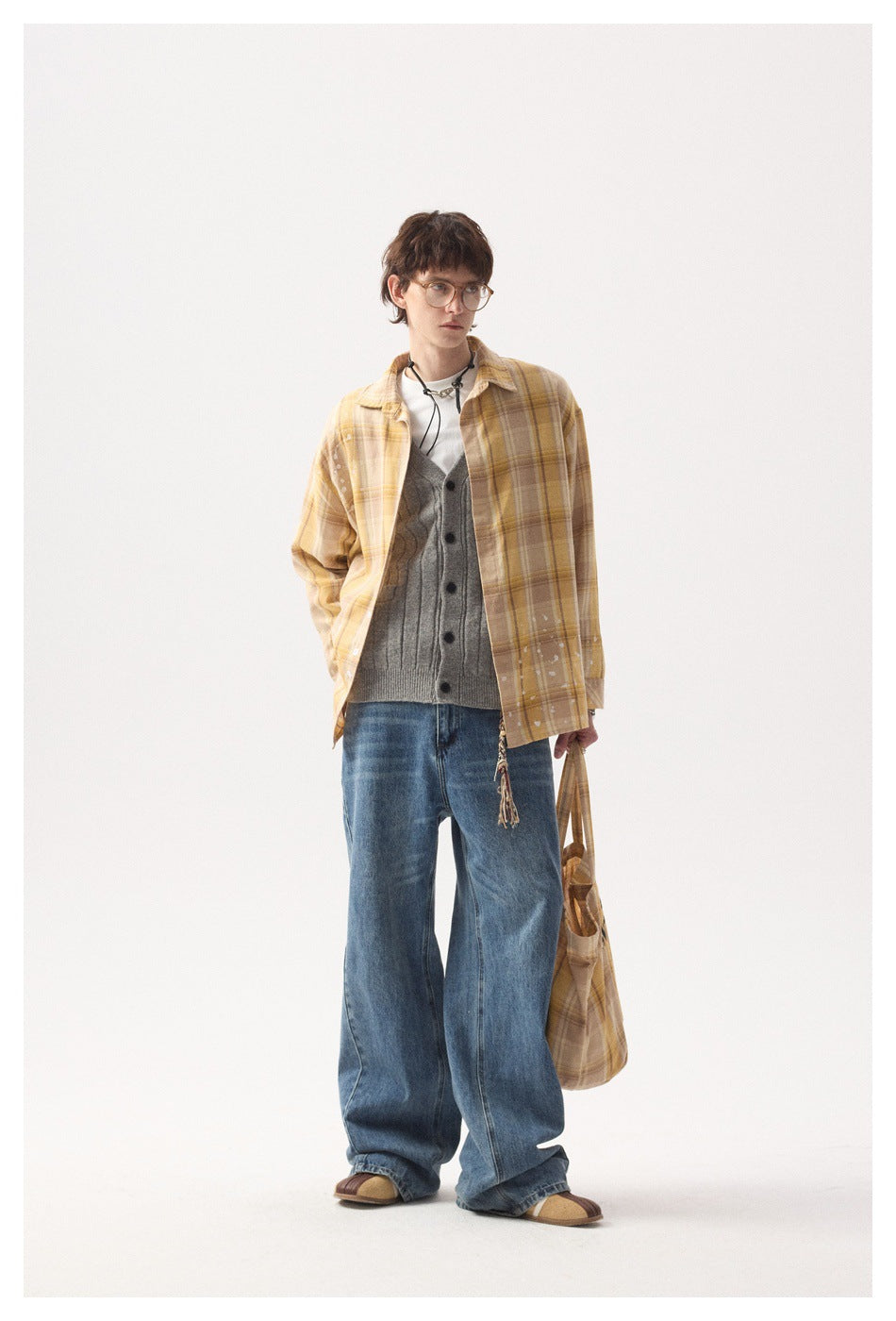 Model wearing the yellow plaid shirt open over a gray cardigan, white tee, wide-leg jeans and a plaid tote