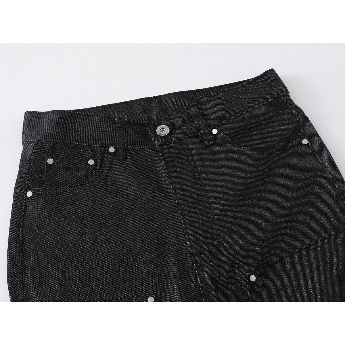 Close-up of black denim pants showing the waistband, button, front pockets, rivets and fly.