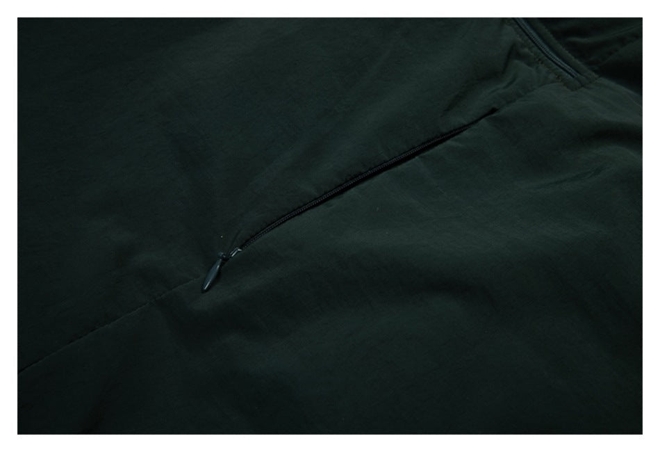 Close-up of a dark green jacket's diagonal zip pocket and zipper pull.