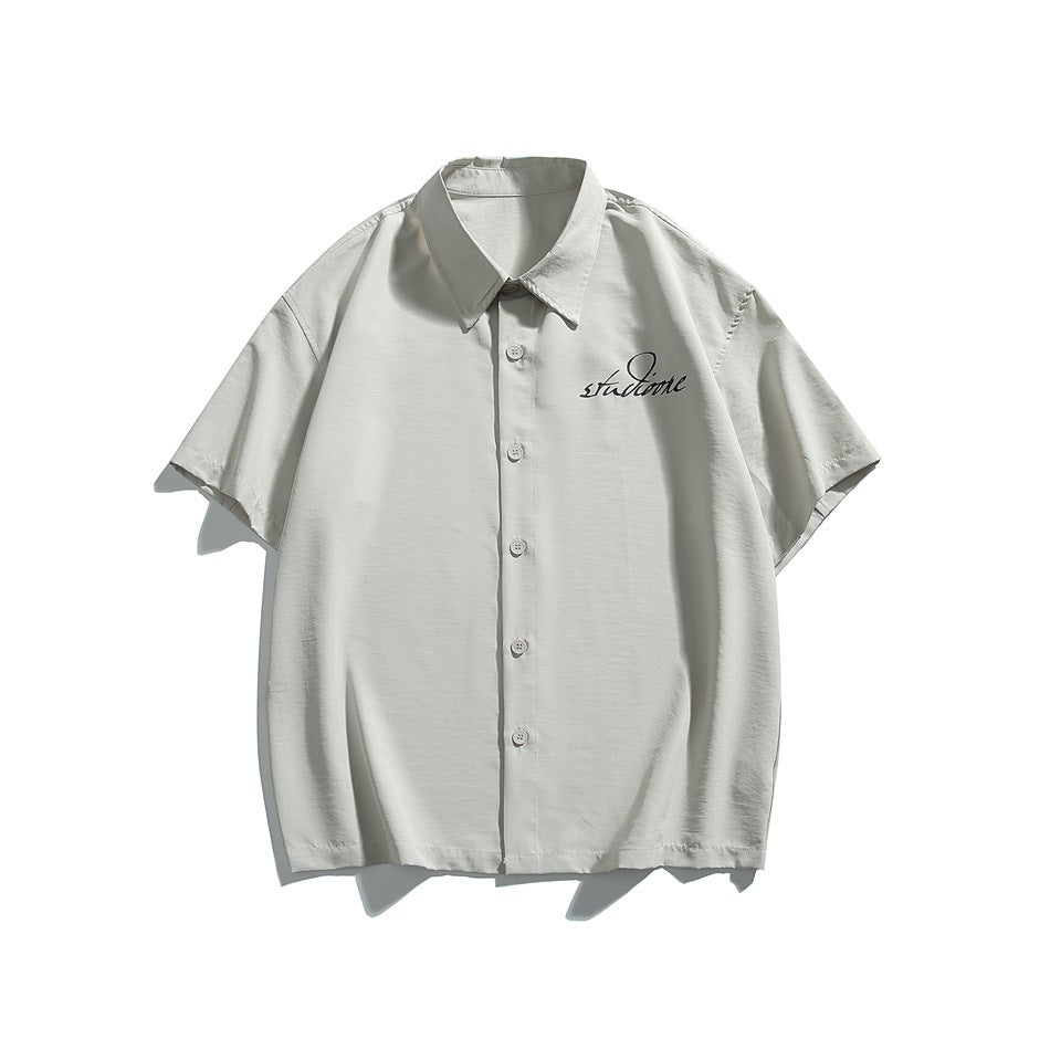 Light gray short-sleeve button-up shirt with black script graphic on the left chest, flat front view