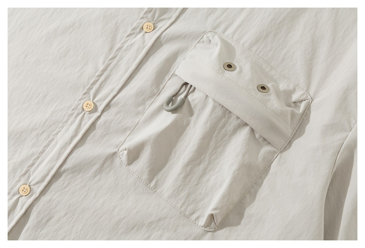 Close-up of an off-white shirt's large flap pocket with metal eyelets and a cord toggle beside the button placket.