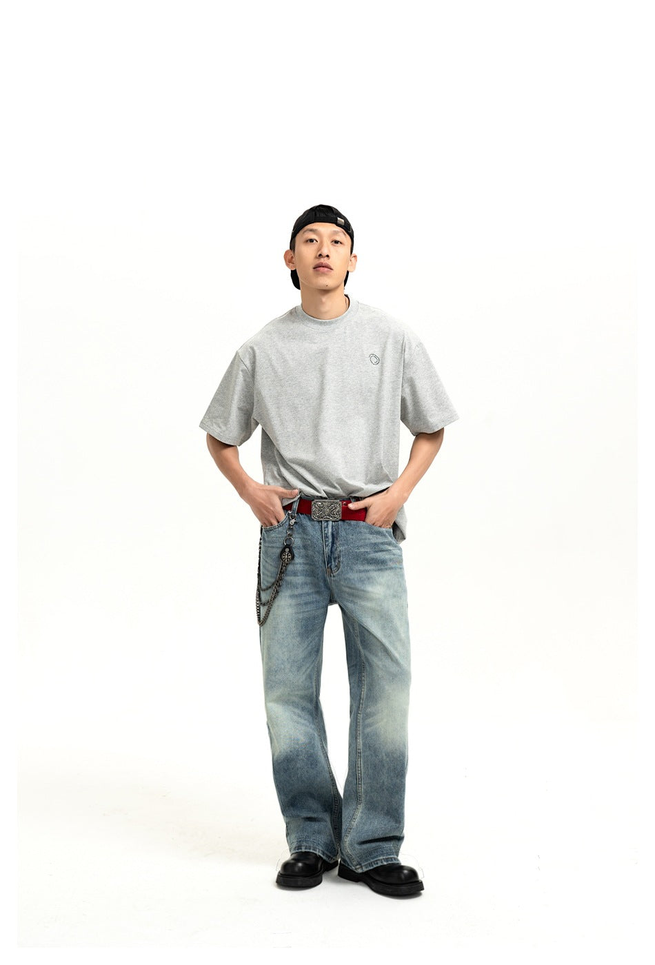 Model wearing a gray short-sleeve T-shirt with small chest logo, blue jeans, red belt and chain