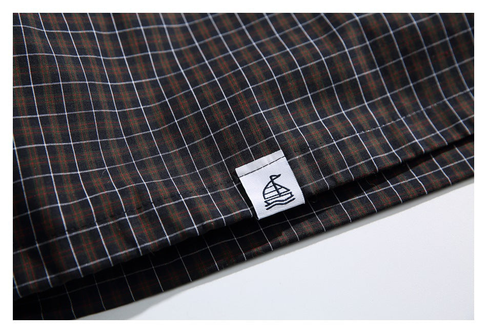 Dark plaid garment hem with a small white tag bearing a sailboat illustration.