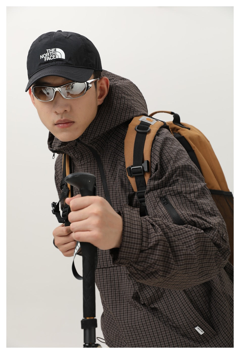 Close-up of the dark brown grid-pattern jacket's hood, high collar, sleeve zipper pocket and front pocket.