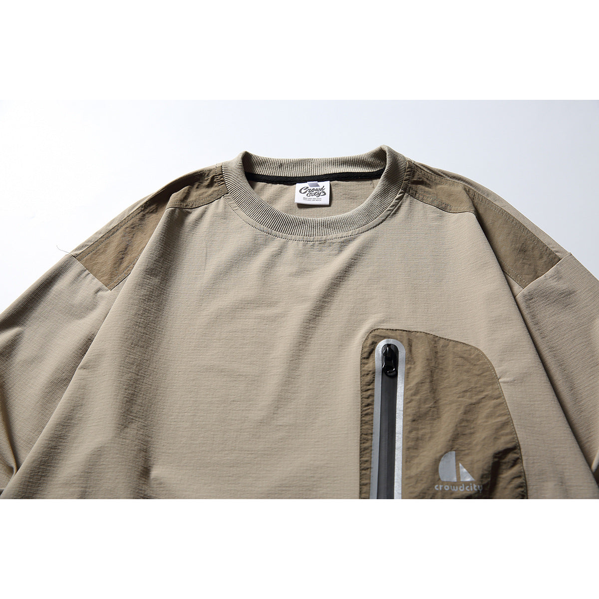 Close-up of a taupe long-sleeve pullover with dark contrast shoulder panels and a zippered chest pocket.