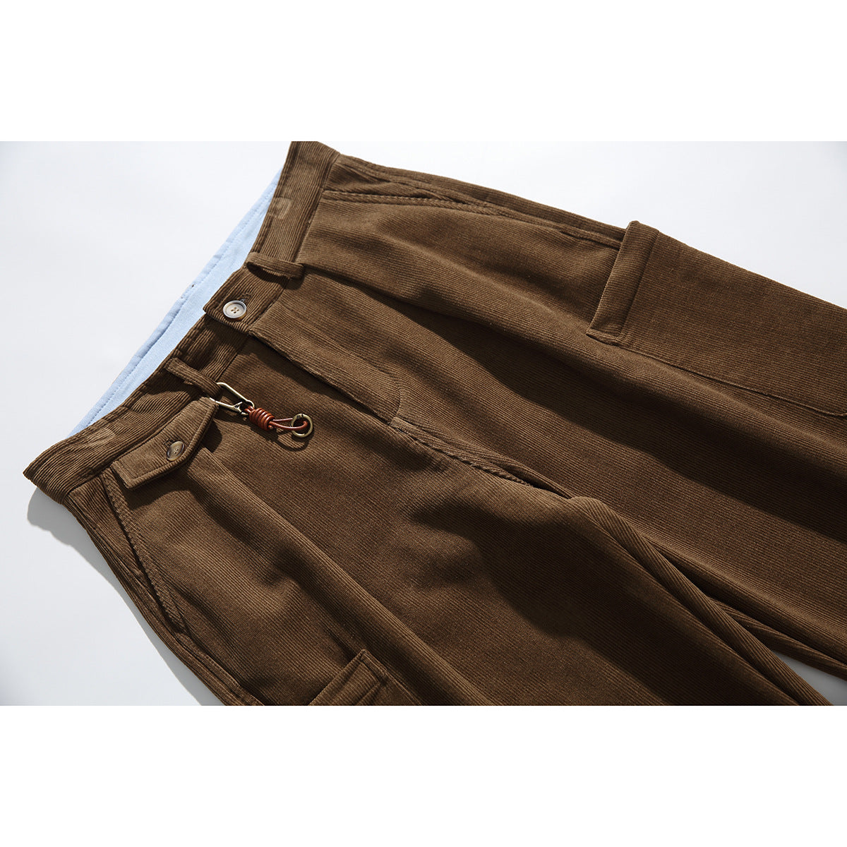 Close-up of brown corduroy trousers showing the waistband, button, front pocket and metal clip detail.