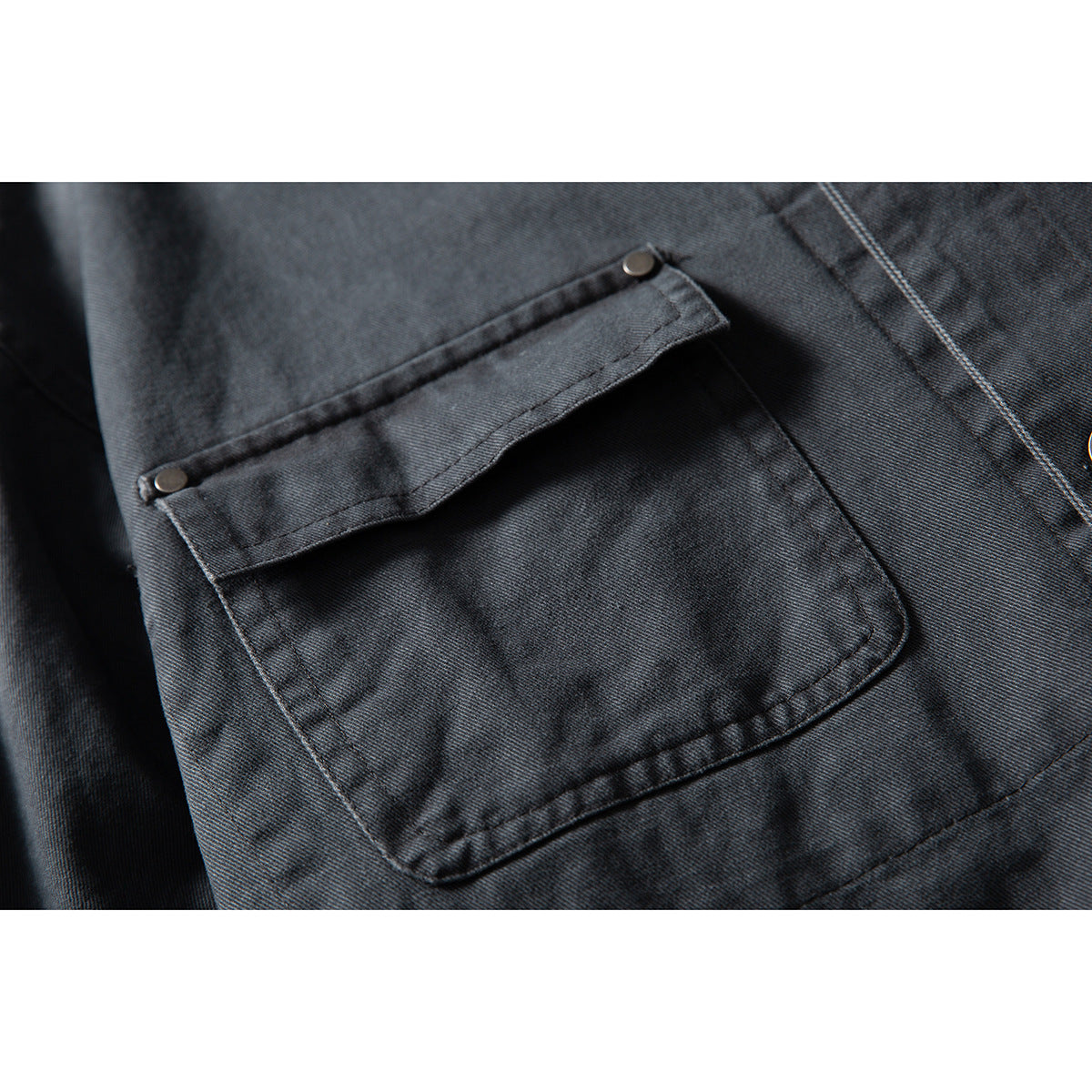 Close-up of a large charcoal jacket pocket with a buttoned flap and visible stitching.