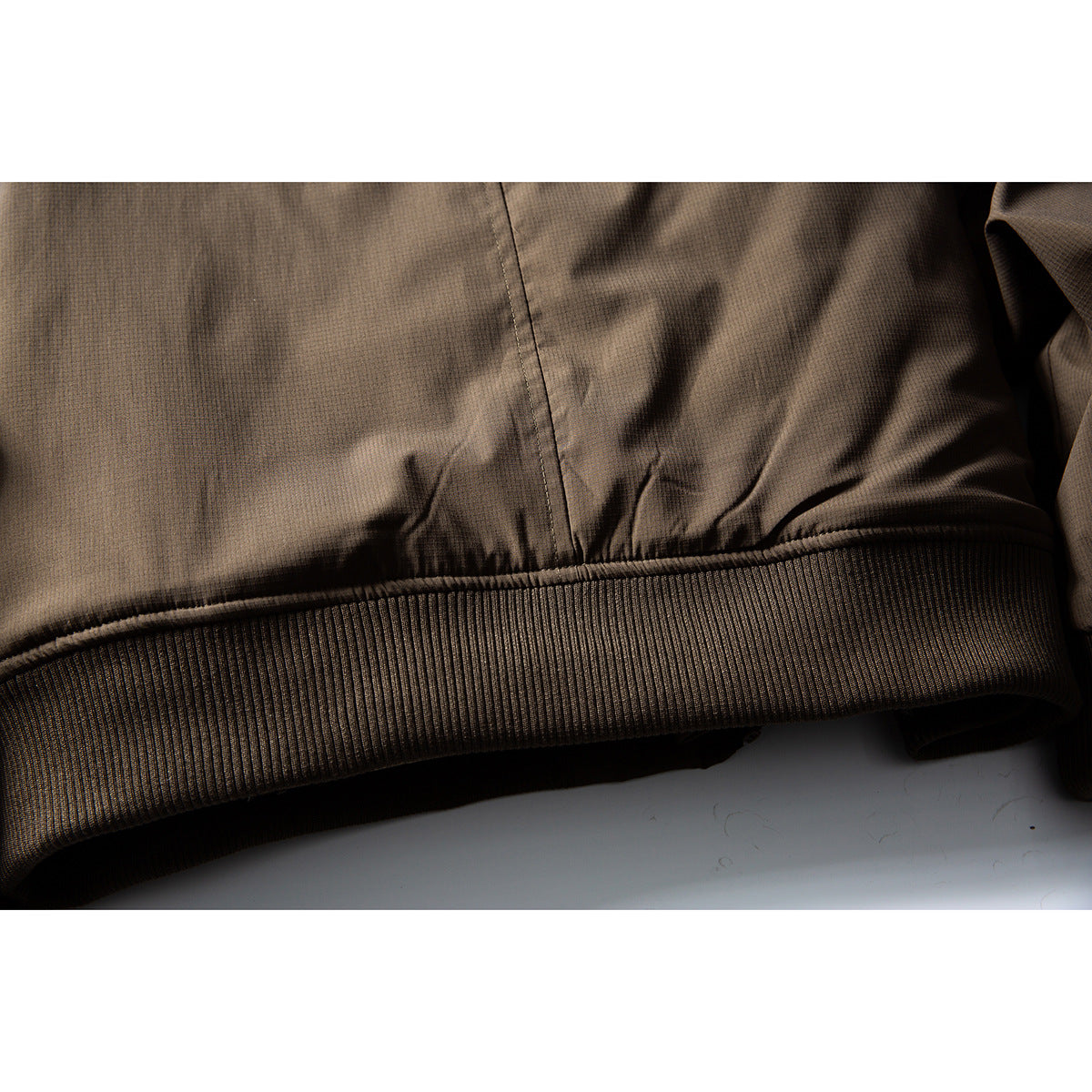 Close-up of the dark brown jacket's ribbed waistband and hem seam.