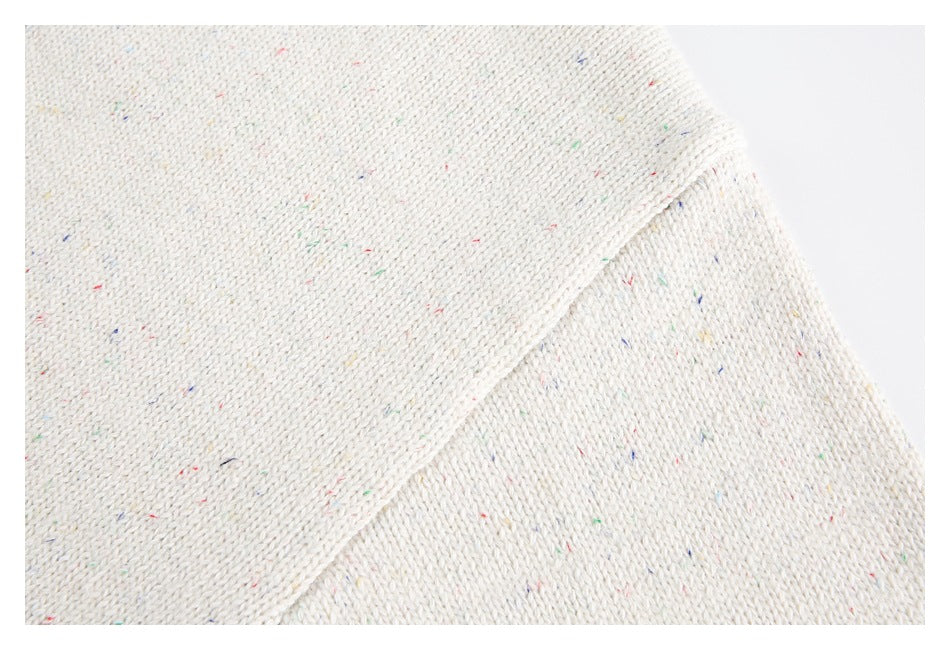 Close-up of cream knit fabric with colorful flecks and a diagonal seam.