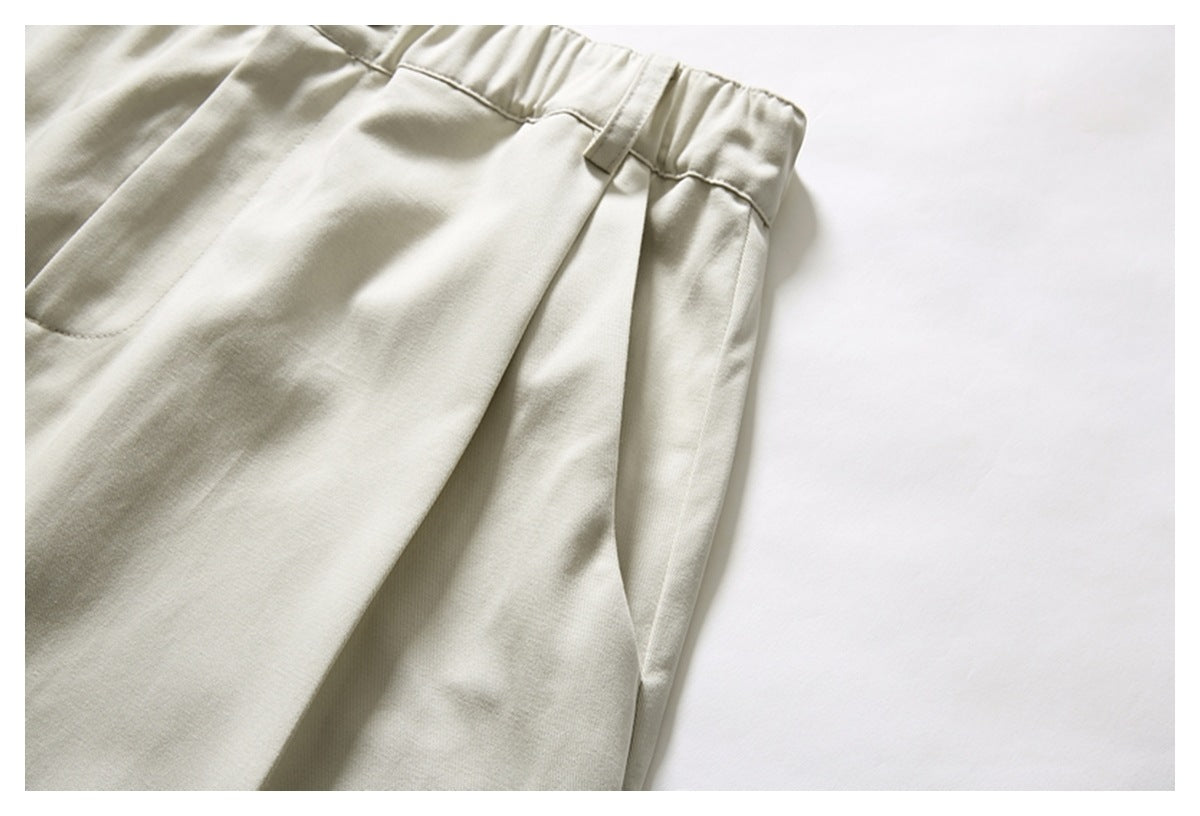Close-up of cream trousers showing an elastic waistband, belt loop, front pleat, and pocket edge.