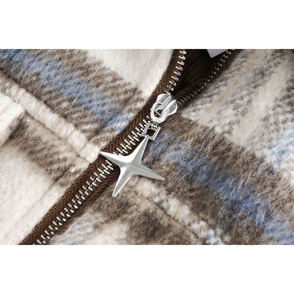 Close-up of a silver star-shaped zipper pull on a brown zipper over cream, gray, and blue plaid fabric.