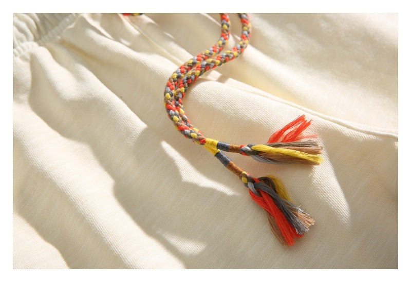 Close-up of multicolored braided drawstrings with tassel ends on the cream shorts.