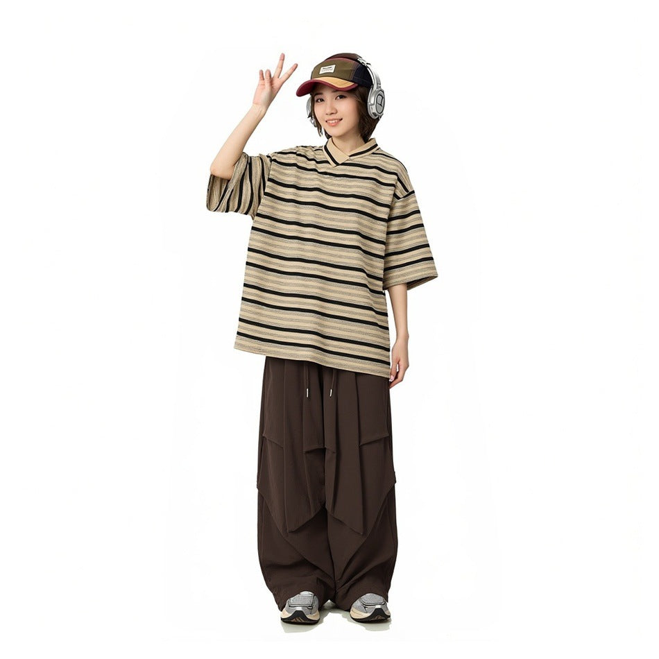 Model wearing a loose beige-and-black striped V-neck shirt with wide dark brown draped trousers.