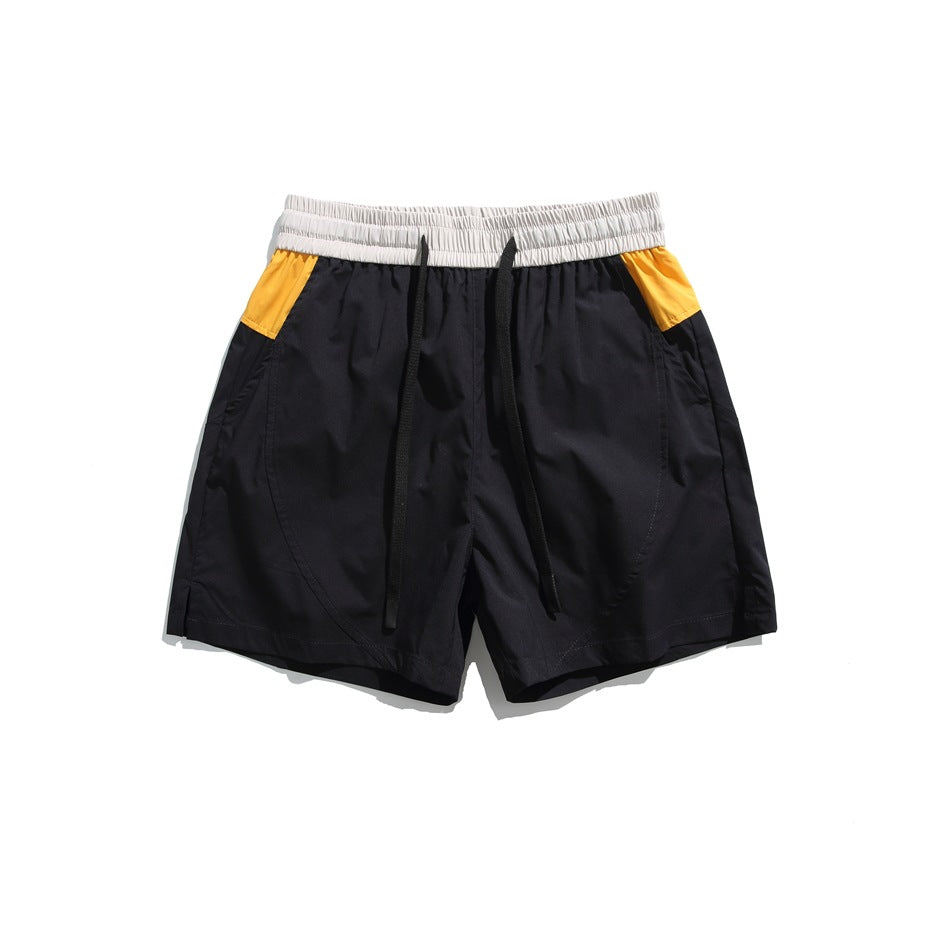 Black drawstring shorts with light gray waistband and orange-yellow side panels, flat lay front view