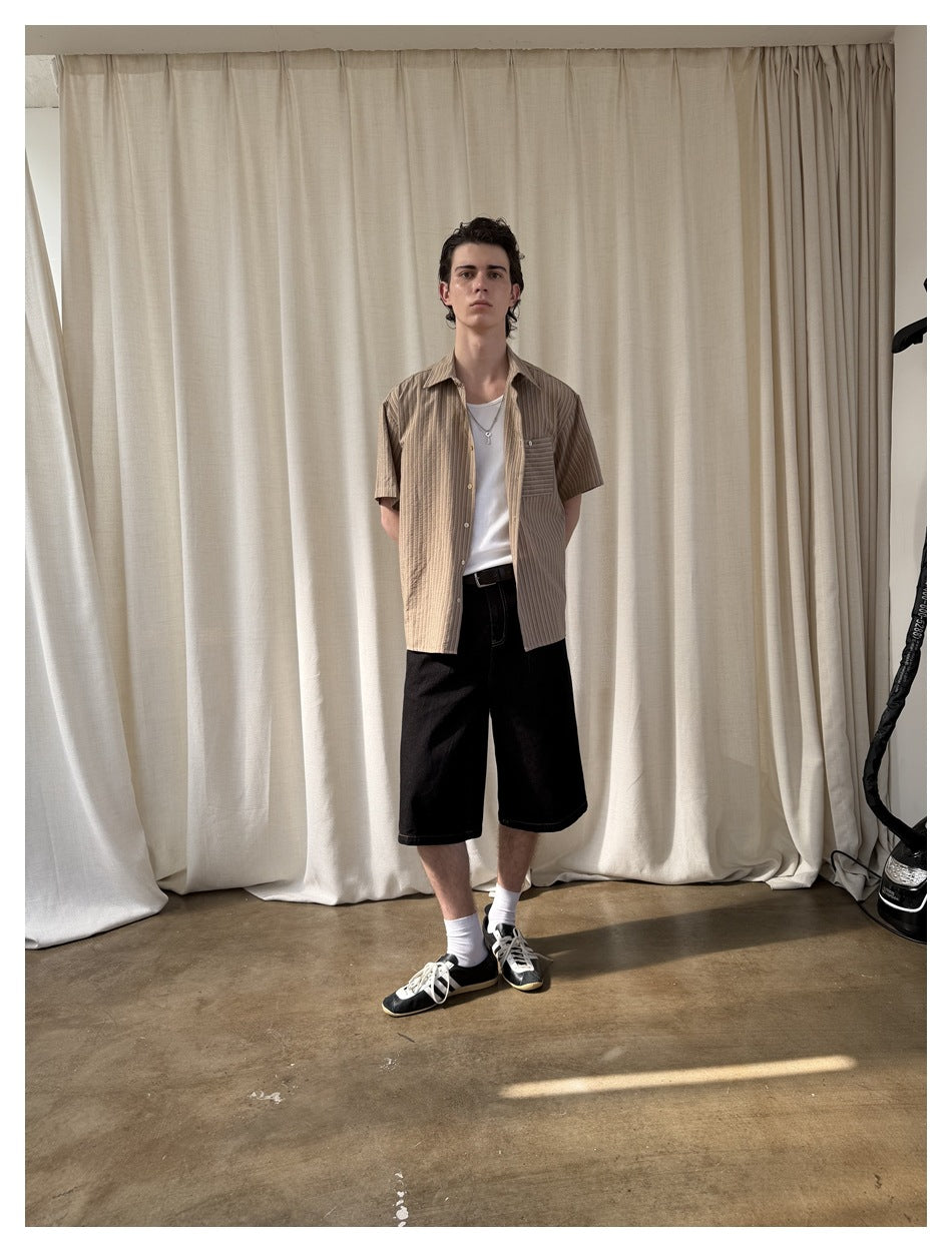Full-length model wearing an open tan striped short-sleeve shirt over a white tee with black shorts.