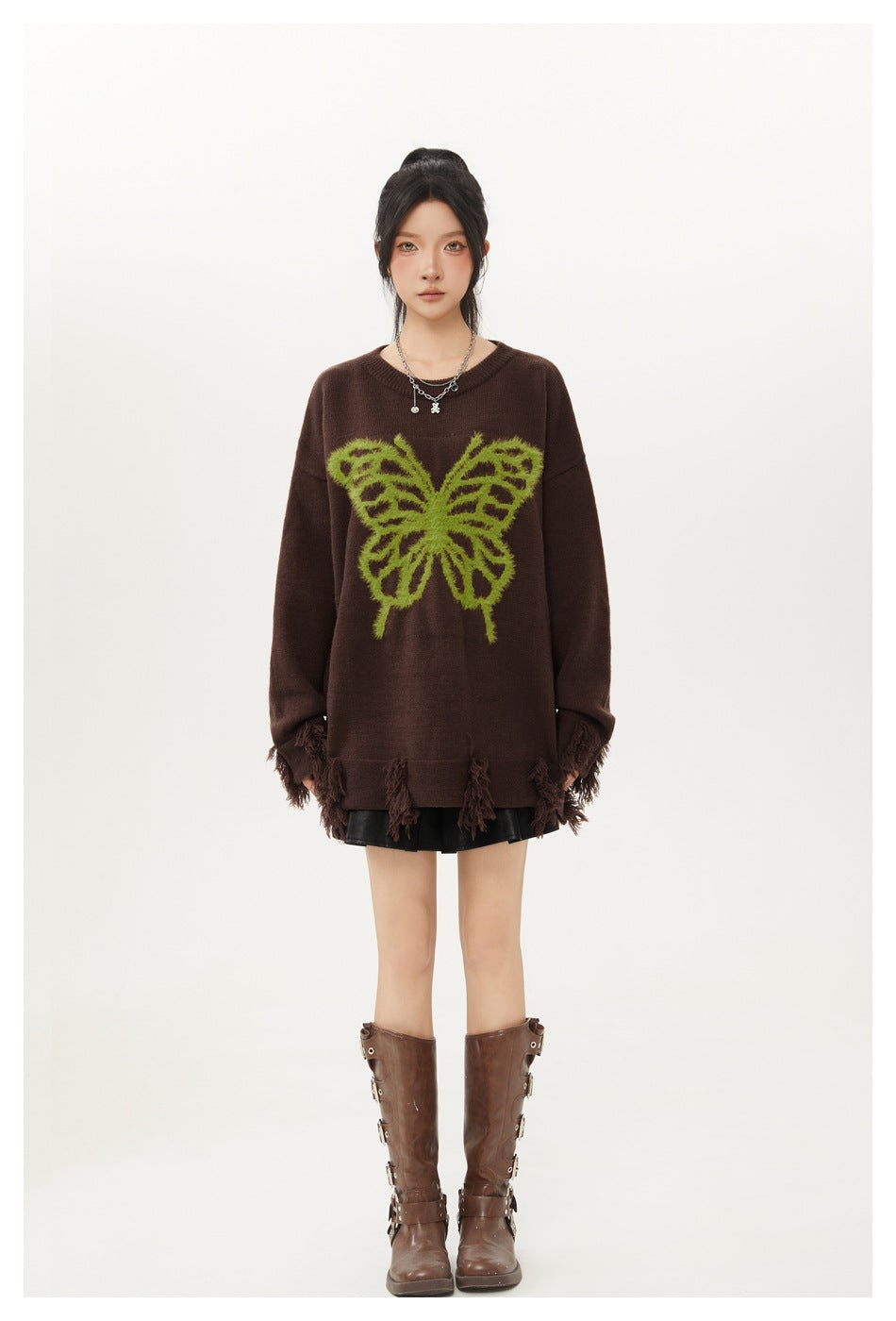 Model wearing an oversized brown butterfly sweater with fringe hem over a black pleated mini skirt and brown boots