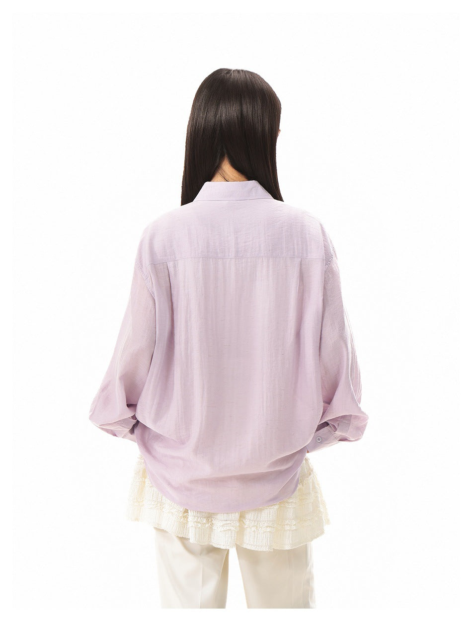 Back view of a model wearing an oversized pale lavender shirt with a yoke seam and long sleeves.