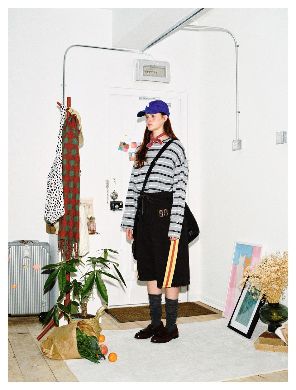 Side view of a model wearing a gray-and-black striped long-sleeve top and black shorts with red and yellow side stripes.