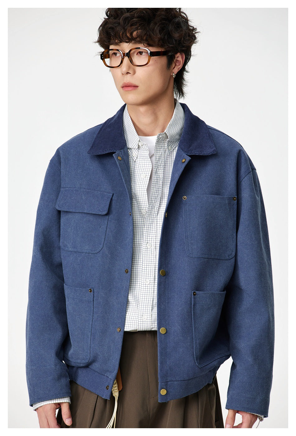 Model wearing a blue utility jacket with a wide collar, snap closure and four large pockets over a checked shirt.