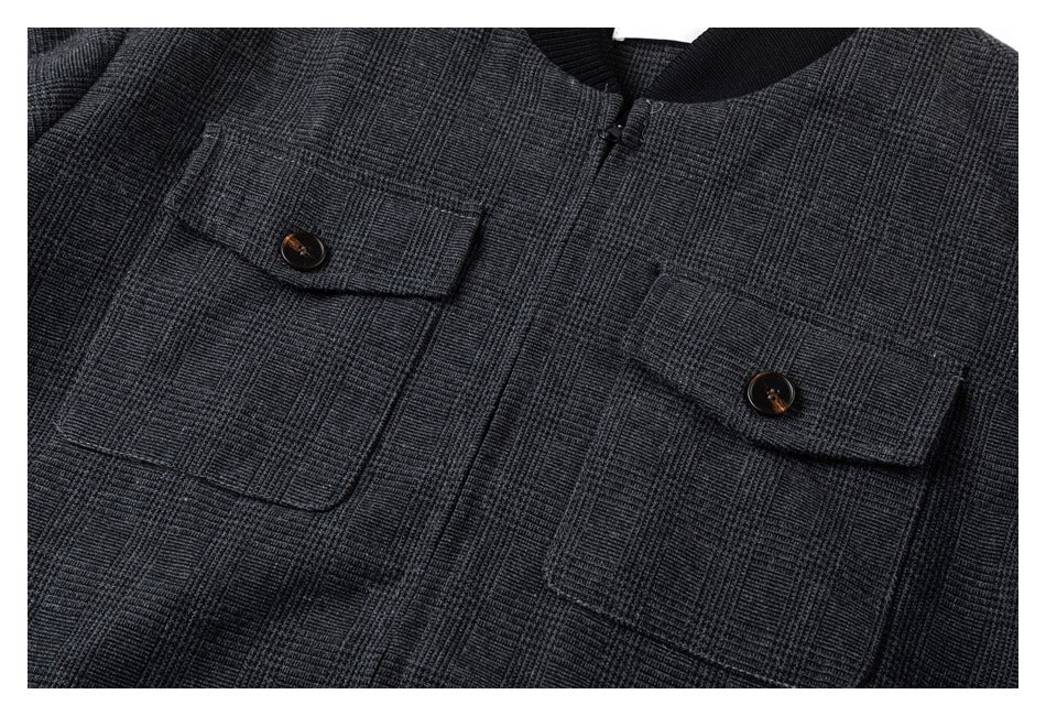 Close-up of a charcoal plaid jacket front with two buttoned flap chest pockets and a black ribbed collar.