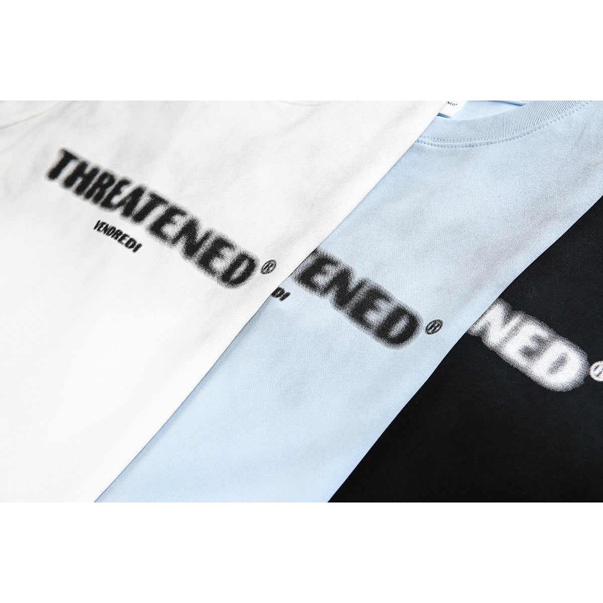 Close-up of white, pale blue, and black T-shirts showing blurred black and white chest lettering.