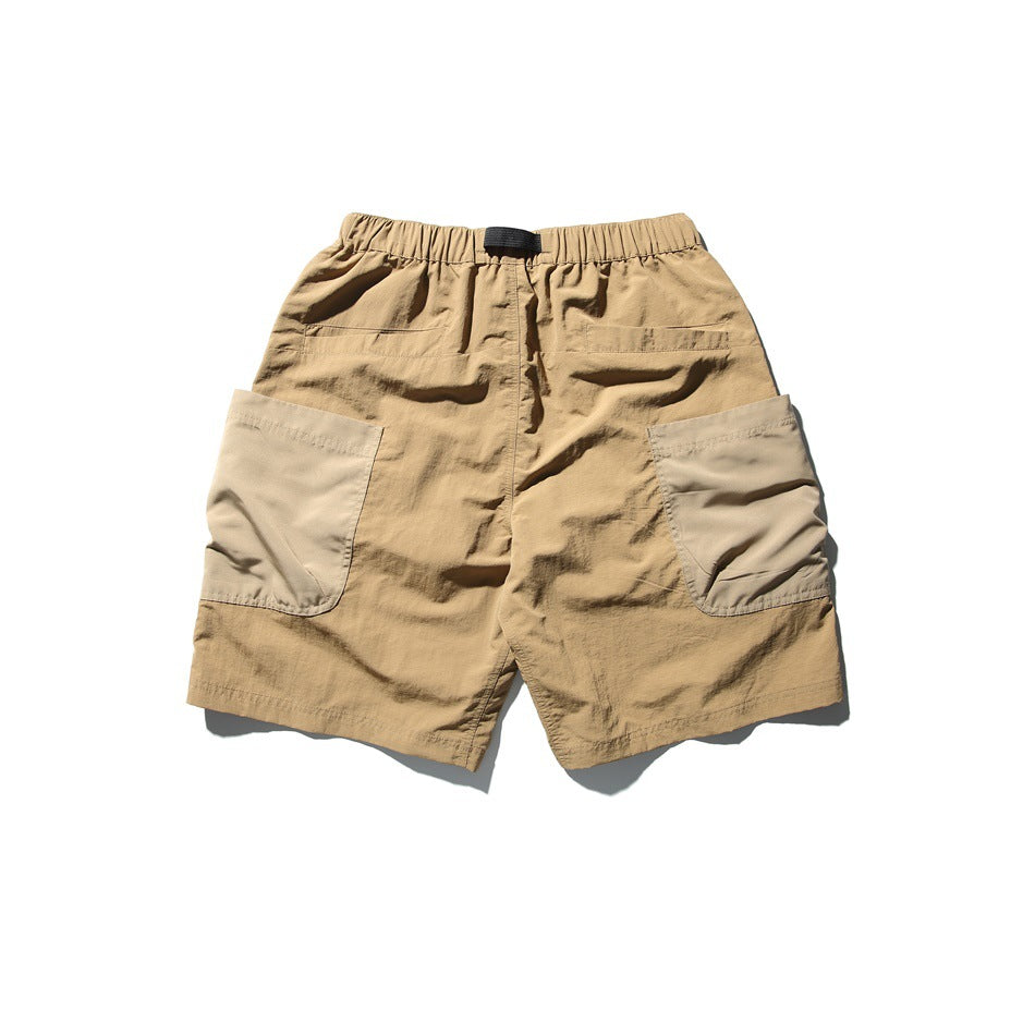Tan utility shorts laid flat, with an elastic waist, black buckle belt, and large light-beige side pockets.